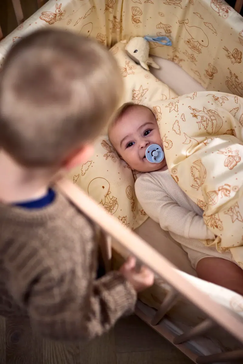 Baby mit Schnuller in Bettwäsche mit Tiermotiven von FILIBABBA, daneben ein Kind