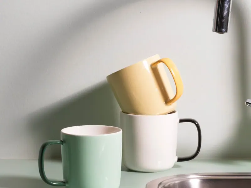 Kaffeebecher von ONA in Mintgrün, Weiß und Gelb neben einer Spüle