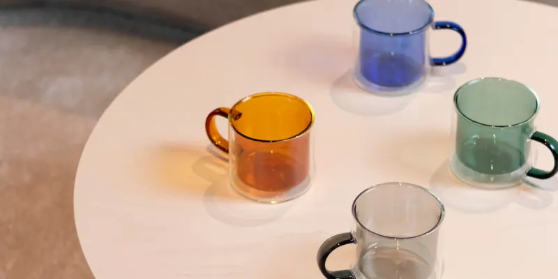 Doppelwandige Glasbecher von ONA in Bernstein, Blau, Grün und Grau auf einem runden Tisch