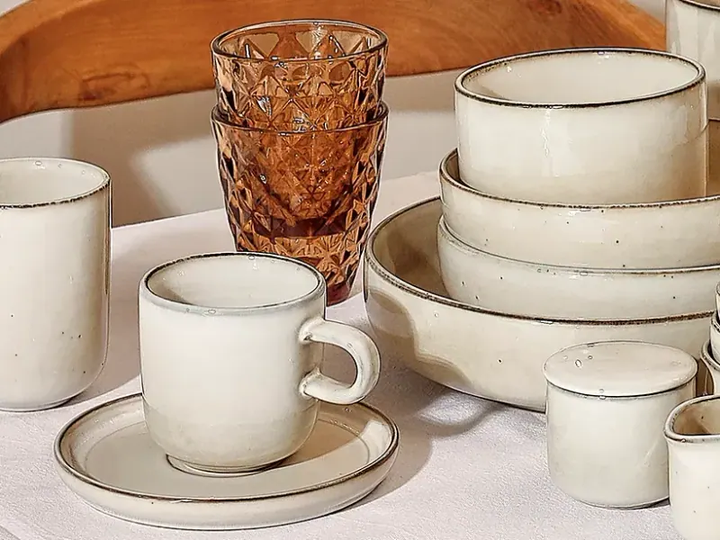 Cremefarbene Schalen, Becher und Tasse mit Untertasse der Salt&Pepper-Serie Meridian auf einem gedeckten Tisch