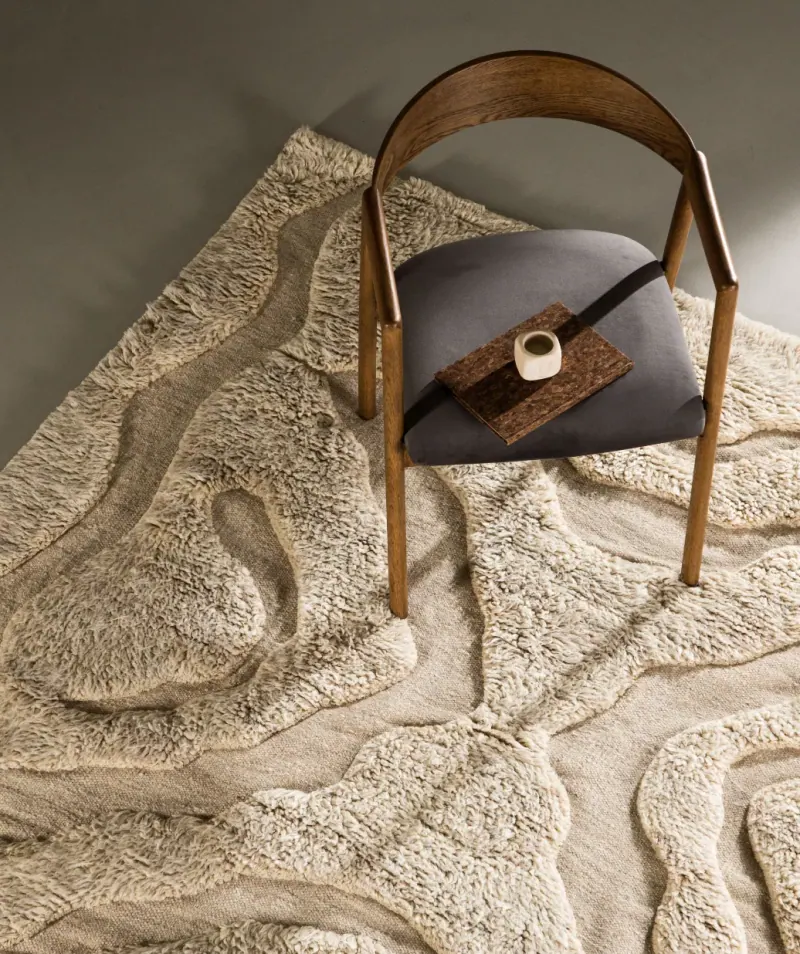 Holzstuhl auf einem hellen Wollteppich mit geschwungenem Reliefmuster