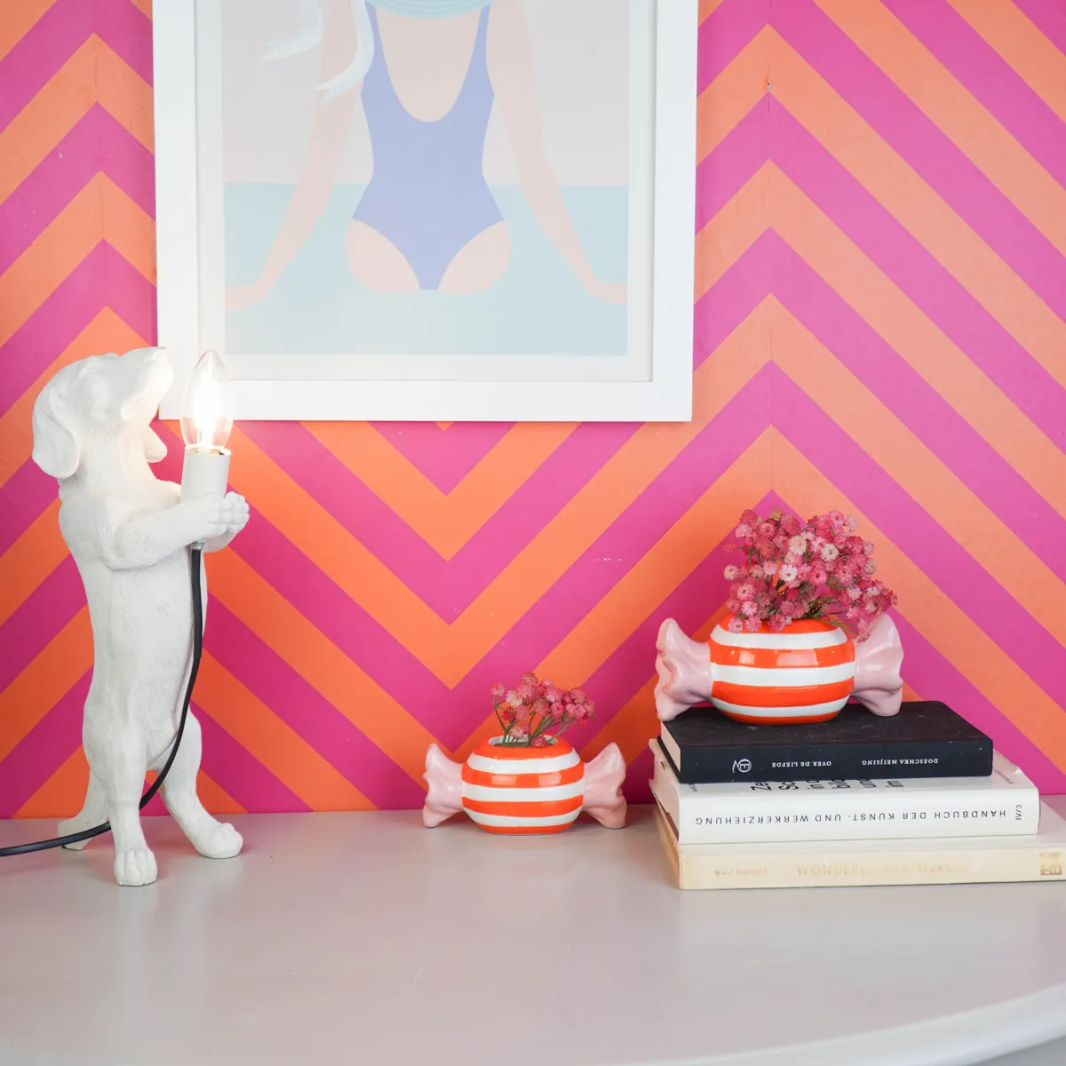 Bunte Deko von Housevitamin auf einem Regal vor einer Wand mit rosa und orangem Zickzackmuster
