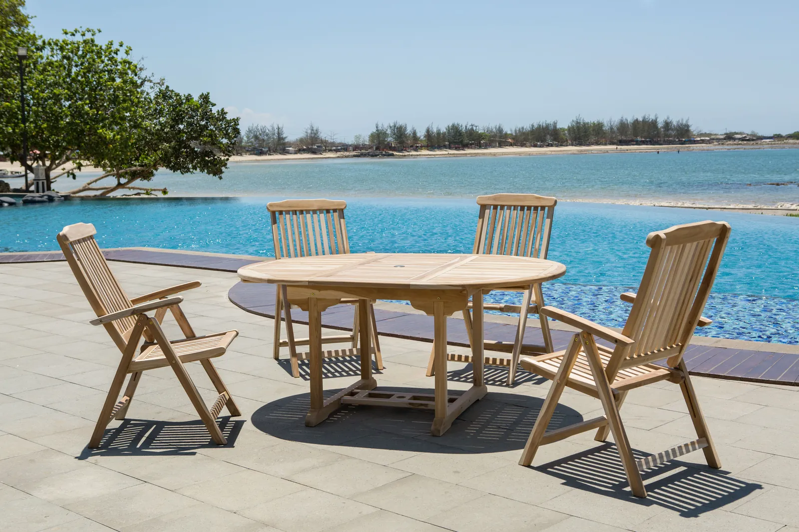 Essgruppe von Möbilia aus Teakholz mit ausziehbarem Tisch und Klappstühlen auf einer Terrasse am Pool
