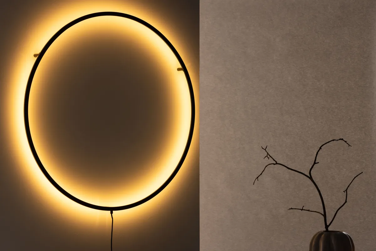 Leuchtende runde Wandleuchte aus der Kollektion VIND x Josefin Lustig neben einem Zweig in der Vase