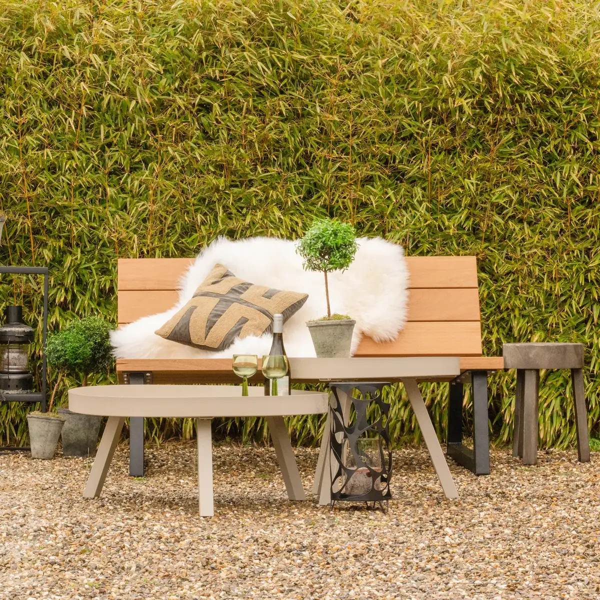 Gartenbank Banco von WOOOD mit Fell und Kissen vor einer Pflanzenwand